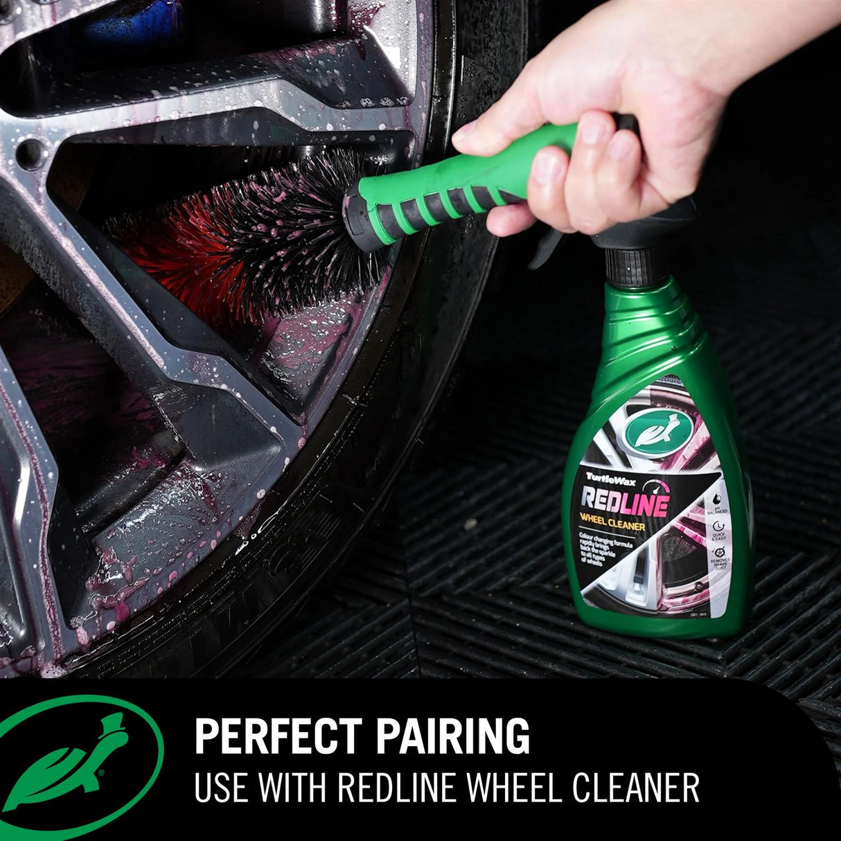 A hand uses a green-handled brush attachment to clean a car wheel, with a green bottle of Professional REDLINE Wheel Cleaner placed on a black textured floor. Text at the bottom reads 'PERFECT PAIRING USE WITH REDLINE WHEEL CLEANER'.