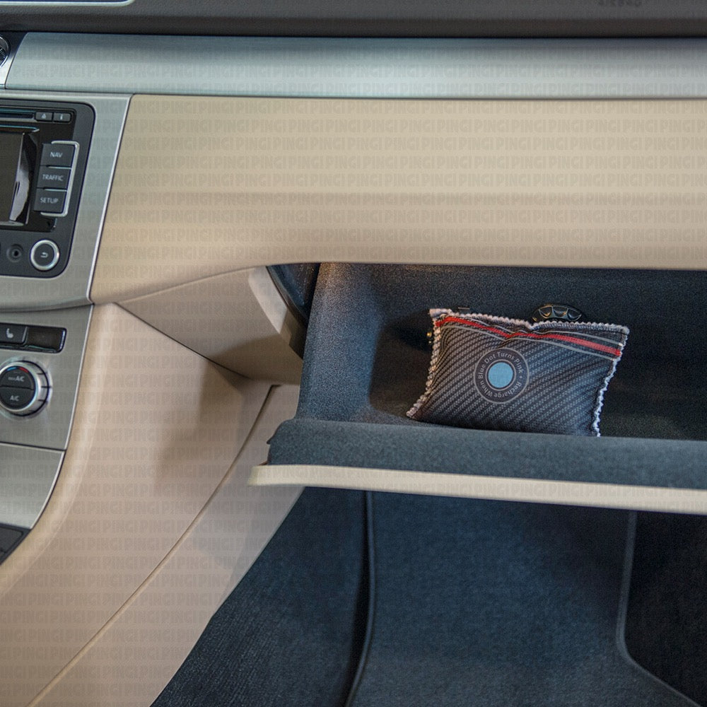 A close-up of a car's glove compartment interior, showing a small textured square air freshener or decorative cushion placed in the open compartment.