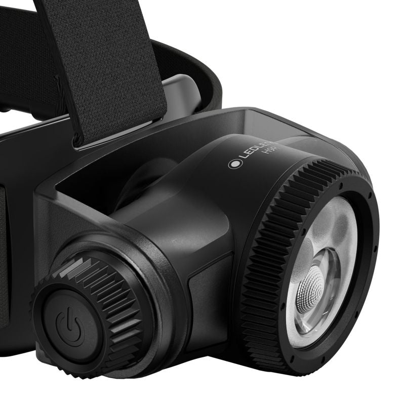 Close-up of a black LED headlamp showing the front lens, adjustment dial, power button, and part of the head strap on a white background.