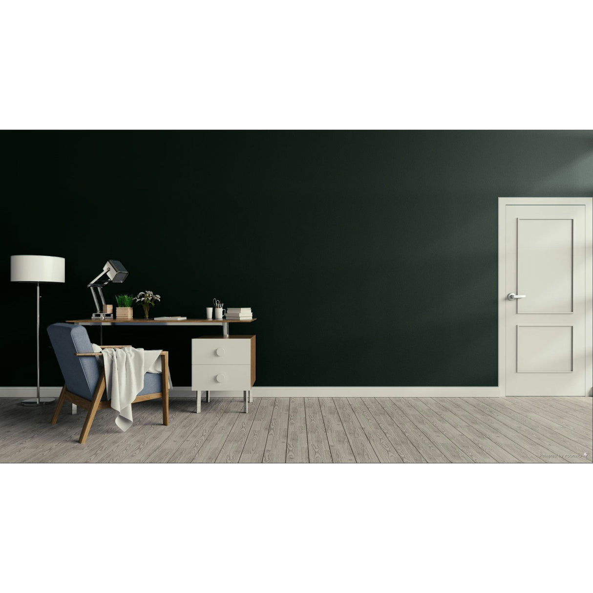 A modern interior room with a dark green wall, light wood floor, a white door on the right, and a home office setup on the left featuring a desk, lamp, chair, and throw blanket.