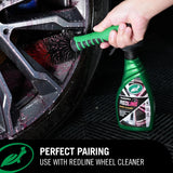 A hand uses a green-handled brush attachment to clean a car wheel, with a green bottle of Professional REDLINE Wheel Cleaner placed on a black textured floor. Text at the bottom reads 'PERFECT PAIRING USE WITH REDLINE WHEEL CLEANER'.