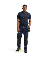 A man modeling a navy blue work shirt and matching navy work pants with black knee panels and a black utility pouch, standing against a solid white background.