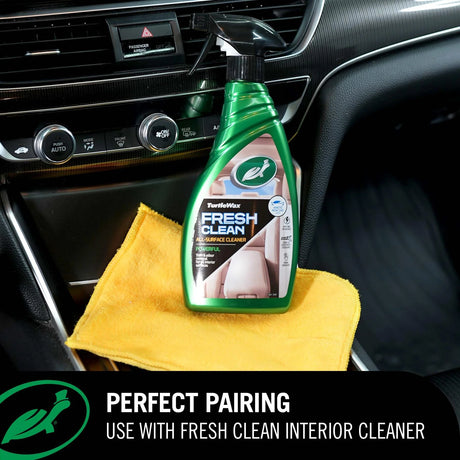 A bottle of Turtle Wax Fresh Clean car interior cleaner placed on a yellow microfiber cloth inside a car console. A black banner at the bottom reads 'PERFECT PAIRING USE WITH FRESH CLEAN INTERIOR CLEANER' with the Turtle Wax logo.