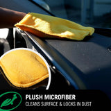 A yellow plush microfiber cleaning cloth being wiped across a black car surface, with a circular inset showing a close-up of the microfiber texture. Text at the bottom reads 'PLUSH MICROFIBER' and 'CLEANS SURFACE & LOCKS IN DUST'.