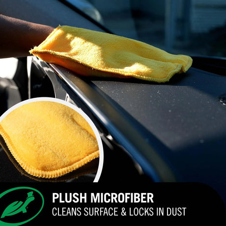 A yellow plush microfiber cleaning cloth being wiped across a black car surface, with a circular inset showing a close-up of the microfiber texture. Text at the bottom reads 'PLUSH MICROFIBER' and 'CLEANS SURFACE & LOCKS IN DUST'.
