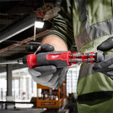 A close-up of a person wearing a high-visibility safety vest and gloves, using a Milwaukee cordless screwdriver with multiple bits attached in an industrial workshop setting.
