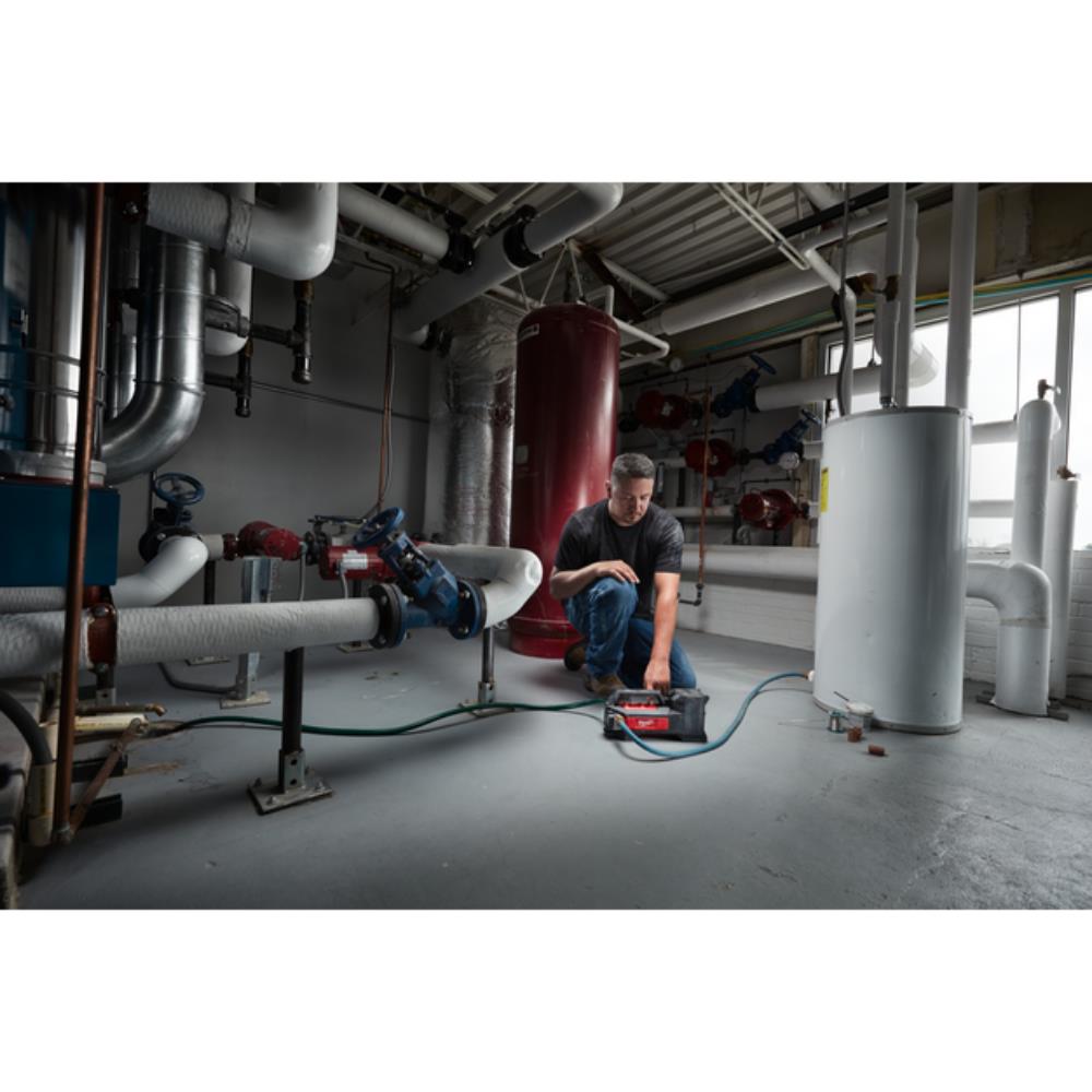 Person working on a piece of equipment in a large industrial setting with pipes and machinery. Milwaukee M18BTP-0 M18 Transfer Pump | Bare Unit