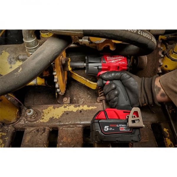 Milwaukee 5V-LITHI+ cordless impact wrench being used by a gloved hand on a rusty piece of industrial machinery.