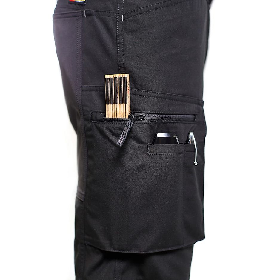 Black pants with multiple pockets and a wooden tool in one of them on a white background. Blaklader 1459 Service Trousers Stretch