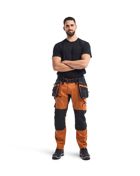 Man wearing a black t-shirt and orange work pants with tool belt on a white background