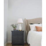 Bedroom with a nightstand featuring a lamp and decorative items, next to a bed with pillows.