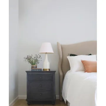 Bedroom with a nightstand featuring a lamp and decorative items, next to a bed with pillows.