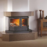 A black wood-burning fireplace insert with glowing orange logs inside, set on a raised speckled stone mantel and base in a living room.