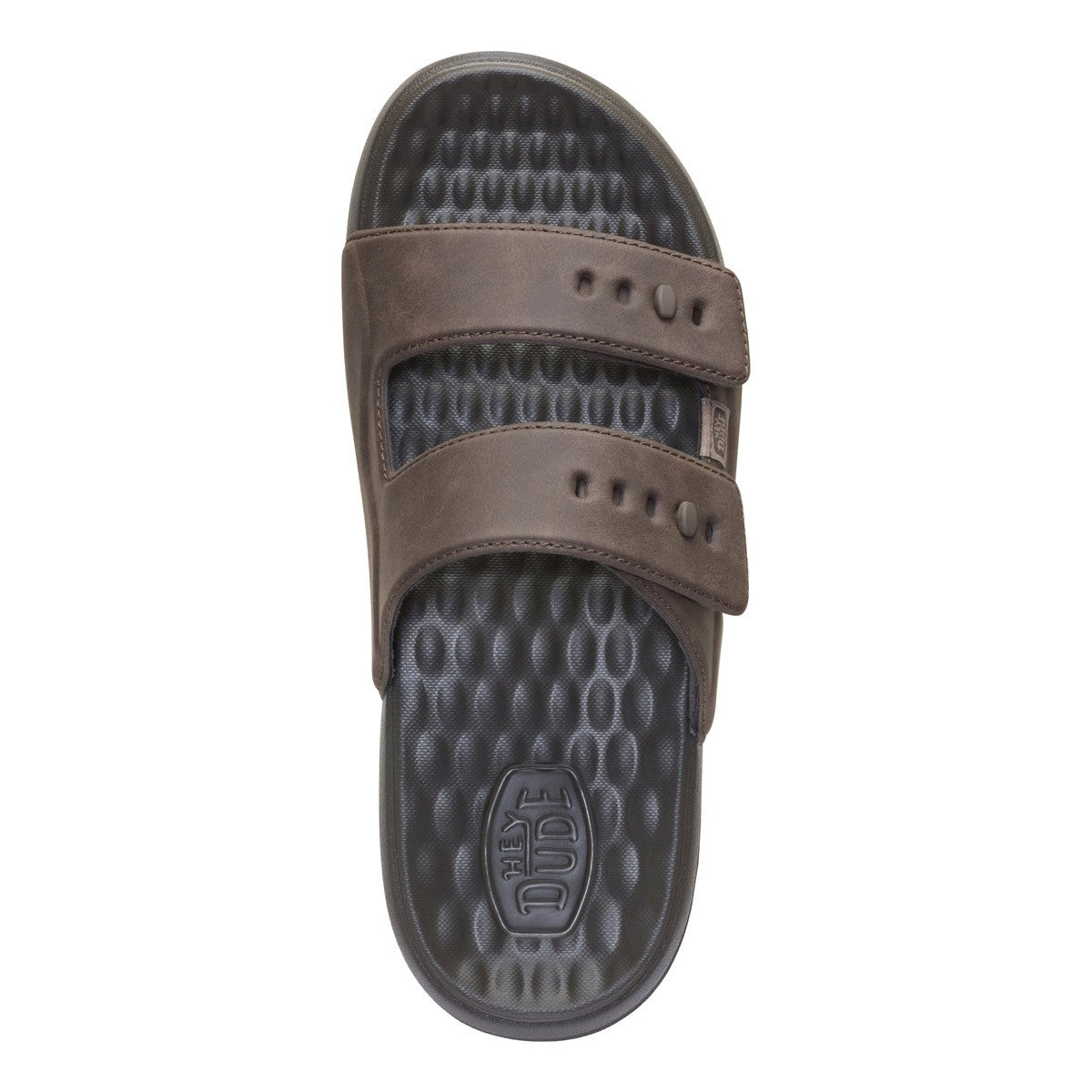 A single brown slide sandal with two adjustable straps and a textured dark gray footbed, shown from a top-down view on a white background. The footbed features an embossed logo that reads 'The Dude'.