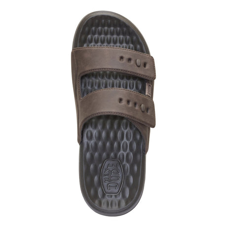 A single brown slide sandal with two adjustable straps and a textured dark gray footbed, shown from a top-down view on a white background. The footbed features an embossed logo that reads 'The Dude'.