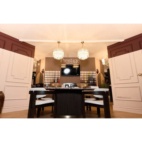 A luxury dining room interior featuring a dark wood dining table with white upholstered chairs, two crystal chandeliers, and a wall-mounted TV displaying the Prestige logo. Prestige Chalking Paint