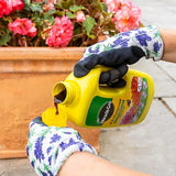 Person wearing gardening gloves pouring a liquid from a Miracle-Gro container into a potted plant.