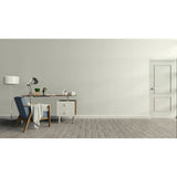 A minimalist interior room with a light beige wall, gray wood floor, a white door on the right, and a home office setup on the left featuring a desk, lamp, chair, and small cabinet. Prestige Foxglove Paint