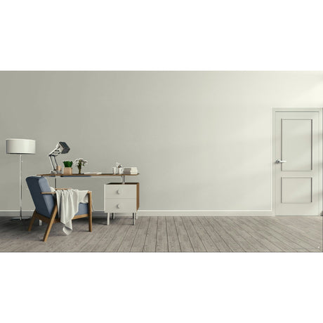 A minimalist interior room with a light beige wall, gray wood floor, a white door on the right, and a home office setup on the left featuring a desk, lamp, chair, and small cabinet. Prestige Foxglove Paint