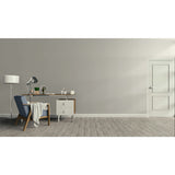 A minimalist room scene with a gray wall, light wood floor, a blue upholstered armchair with a draped throw, a wooden desk with a lamp and small accessories, a white floor lamp, and a white door on the right.
Prestige Letterpress Paint