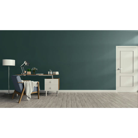 A modern room scene with a dark teal-green wall, light wood plank flooring, a white door on the right, and a home office setup on the left featuring a desk, lamp, chair, and throw blanket.