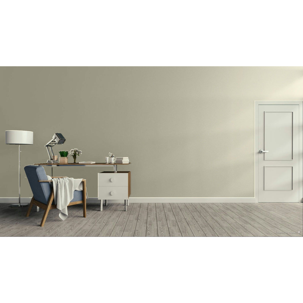 A minimalist interior room with a beige wall, gray wood floor, a white door on the right, and a home office setup on the left featuring a desk, lamp, chair, and throw blanket.