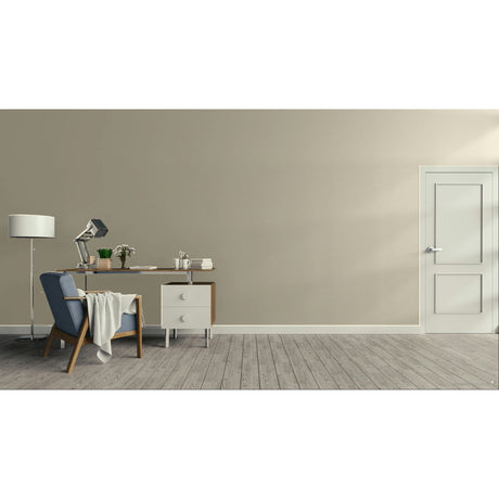 A minimalist room scene with a beige wall, gray wood floor, a blue armchair with a draped throw, a wooden desk with a lamp and small accessories, and a white door on the right.
