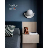 A Prestige Fine Furnishings Schumacher 100 wall sconce in a modern bedroom setting, mounted on a dark slate blue wall above a light wood floating nightstand.