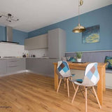 A modern kitchen and dining area with blue walls, light wood flooring, a wooden dining table, and two chairs with blue, beige, and brown geometric patterned upholstery.