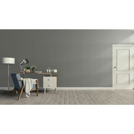 A minimalist room scene with a gray wall, light wood floor, white door, desk, chair, lamp, and small cabinet.