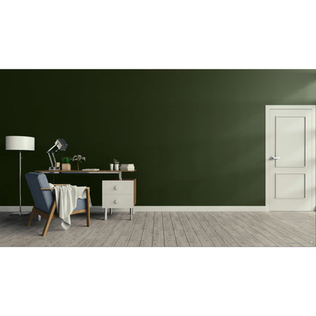 A modern interior room with a dark green wall, light wood floor, a white door on the right, and a home office setup on the left featuring a blue armchair, desk, lamp, and small cabinet.