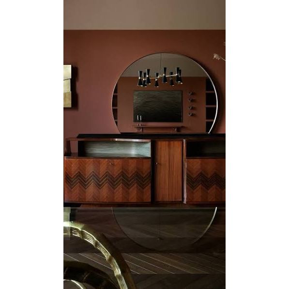 A mid-century modern wooden console cabinet with chevron inlay, a large round wall mirror, and shelving, set against a terracotta-colored wall.