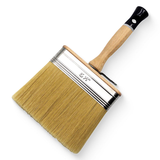 A wide paint brush with natural tan bristles, a silver metal ferrule, and a light wood handle with a black end cap, shown on a plain white background.