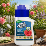 A bottle of Rose Clear Ultra Shield rose and flower spray stands on a wooden table in a garden setting, surrounded by roses, a watering can, gloves, and a trowel.