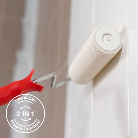 A close-up of a two-in-one paint roller with a red handle applying a white primer and topcoat to a white tiled wall. A circular badge on the bottom left highlights the 'Two In One 2 In 1 Primer + Topcoat' feature. Tikkurila Ceramic Tiles - Kitchen and Bathroom Tile Paint