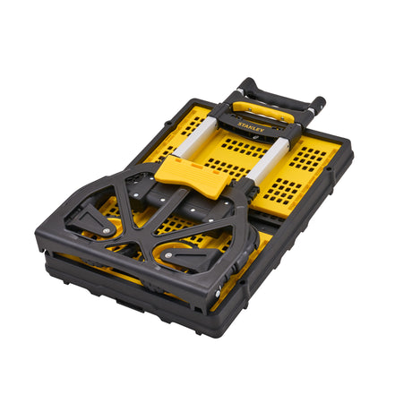 A folded Stanley tool cart with a black plastic frame, yellow perforated plastic base, and silver telescoping handle on a white background.