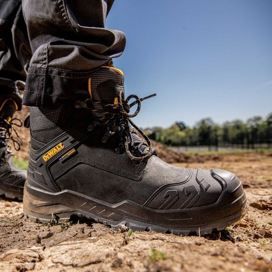Black DeWalt boot on a dirt ground with a blurred natural background