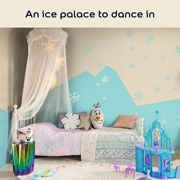 A children's bedroom styled like an ice palace, featuring a bed with a white canopy, Elsa-themed pillows, a blue castle toy, and a wall mural of snowy mountains and snowflakes. The text at the top reads 'An ice palace to dance in'.