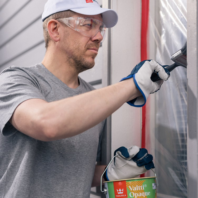A man wearing safety glasses, a white cap, and work gloves applies a brush to a clear protective sheet on a window or door, holding a green and white bucket of Valti Opaque paint.
Buy Tikkurila Valtti Opaque exterior wood paint online at Ted Johnsons. Durable semi-matt finish with excellent weather protection. Fast delivery Ireland.