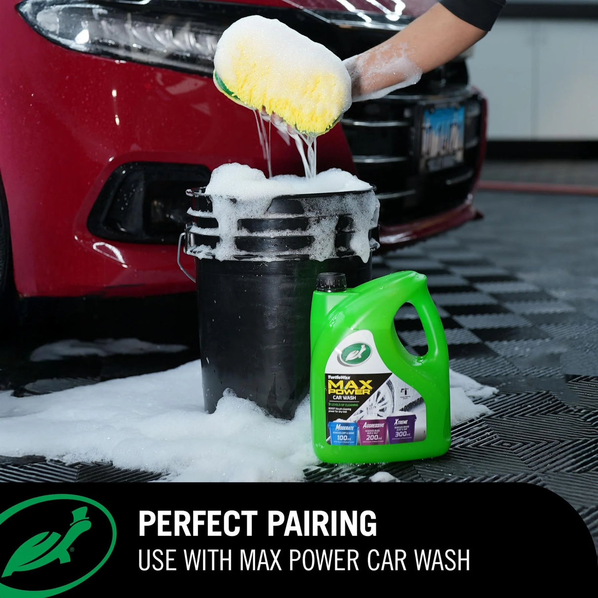 A green bottle of car wash liquid stands next to a black bucket filled with soapy water, with a person using a yellow sponge to scrub a red car in a garage setting. Text at the bottom reads 'PERFECT PAIRING USE WITH MAX POWER CAR WASH'. Turtle Wax M.A.X Power™ 3-in-1 Wash Pad