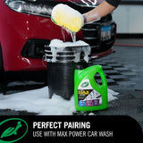A green bottle of car wash liquid stands next to a black bucket filled with soapy water, with a person using a yellow sponge to scrub a red car in a garage setting. Text at the bottom reads 'PERFECT PAIRING USE WITH MAX POWER CAR WASH'. Turtle Wax M.A.X Power™ 3-in-1 Wash Pad