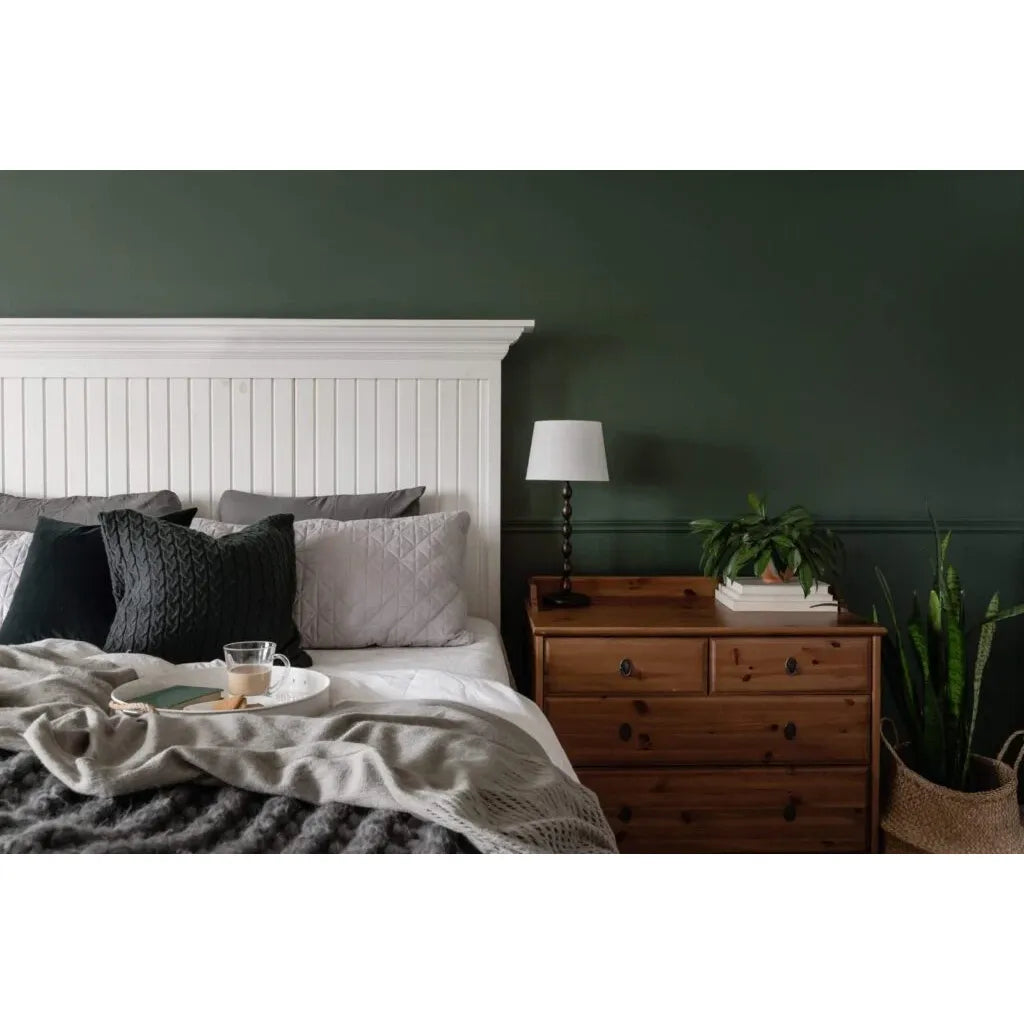 Cozy bedroom with a bed, nightstand, and lamp against a dark green wall.