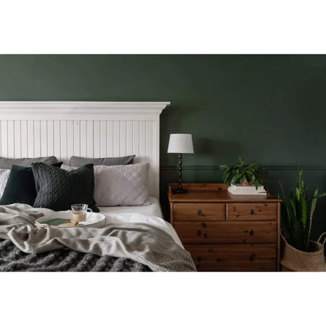 Cozy bedroom with a bed, nightstand, and lamp against a dark green wall.