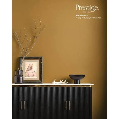 Prestige Side Car A styled interior scene showing a black ribbed cabinet against a warm mustard-yellow wall, with decorative branches, a framed print, a white bowl, and a white antler sculpture. The words 'Prestige' and 'Wall: Slide Our T7' appear in the upper right.