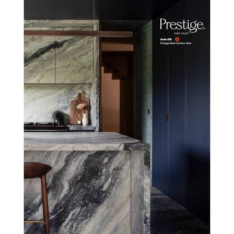 Prestige Ando
A modern kitchen interior featuring a large marble island and matching marble cabinetry in a green, gray, and white veined pattern, alongside dark navy cabinets and a wooden stool. The Prestige Elite Paint brand logo is visible in the top right corner.