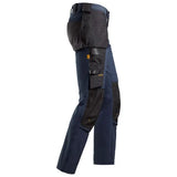 Work pants in navy blue and black, featuring multiple utility pockets, reinforced knee panels, and a high waist with a belt, shown from a side profile on a white background. Snickers 6271 AllroundWork Full Stretch Trousers Holster Pockets