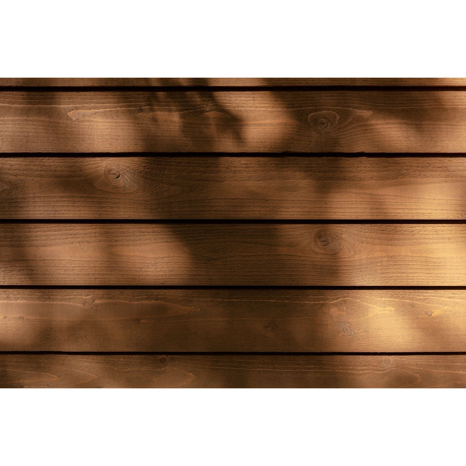 Horizontal wooden planks in warm medium brown tones with soft dappled shadows cast across the surface.
A can of Tikkurila Valtti Plus Color durable wood stain, featuring a label with a wood-grain pattern and a red brand logo block on a white. 
background. Tikkurila Valtti Plus Colour  - Woodstain in Matt Finish