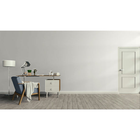 A minimalist room scene with a light gray wall, grey wood floor, a white door on the right, and a furnished left side with a blue armchair, desk, lamp, and small cabinet. Prestige Kensington Grey Pale Paint