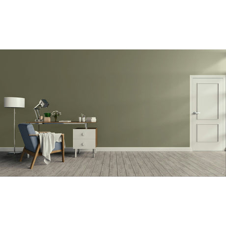 A minimalist room scene with a muted sage green wall, light wood floor, a white door on the right, and a home office setup on the left featuring a desk, lamp, chair, and small cabinet. Prestige Beau Paint