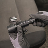 Person wearing gloves holding a black tool with a blurred background